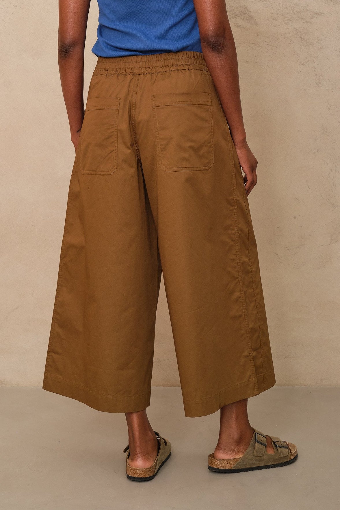 Person wearing brown wide-leg pants and a blue top against a beige background