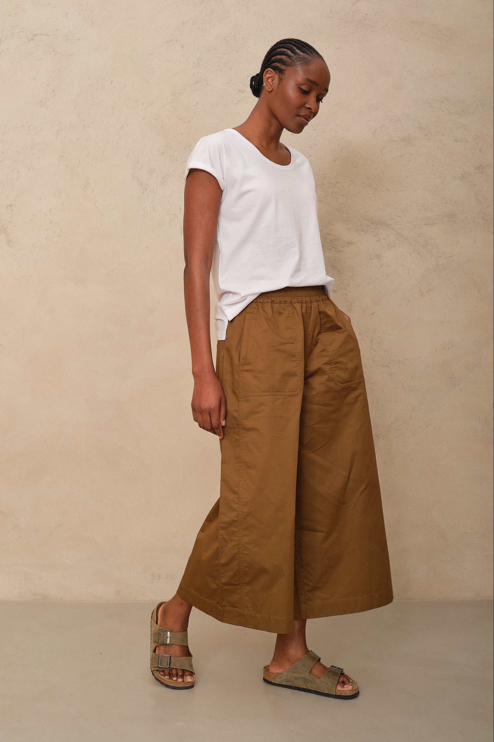 Woman wearing a white t-shirt and brown wide-leg pants against a beige background