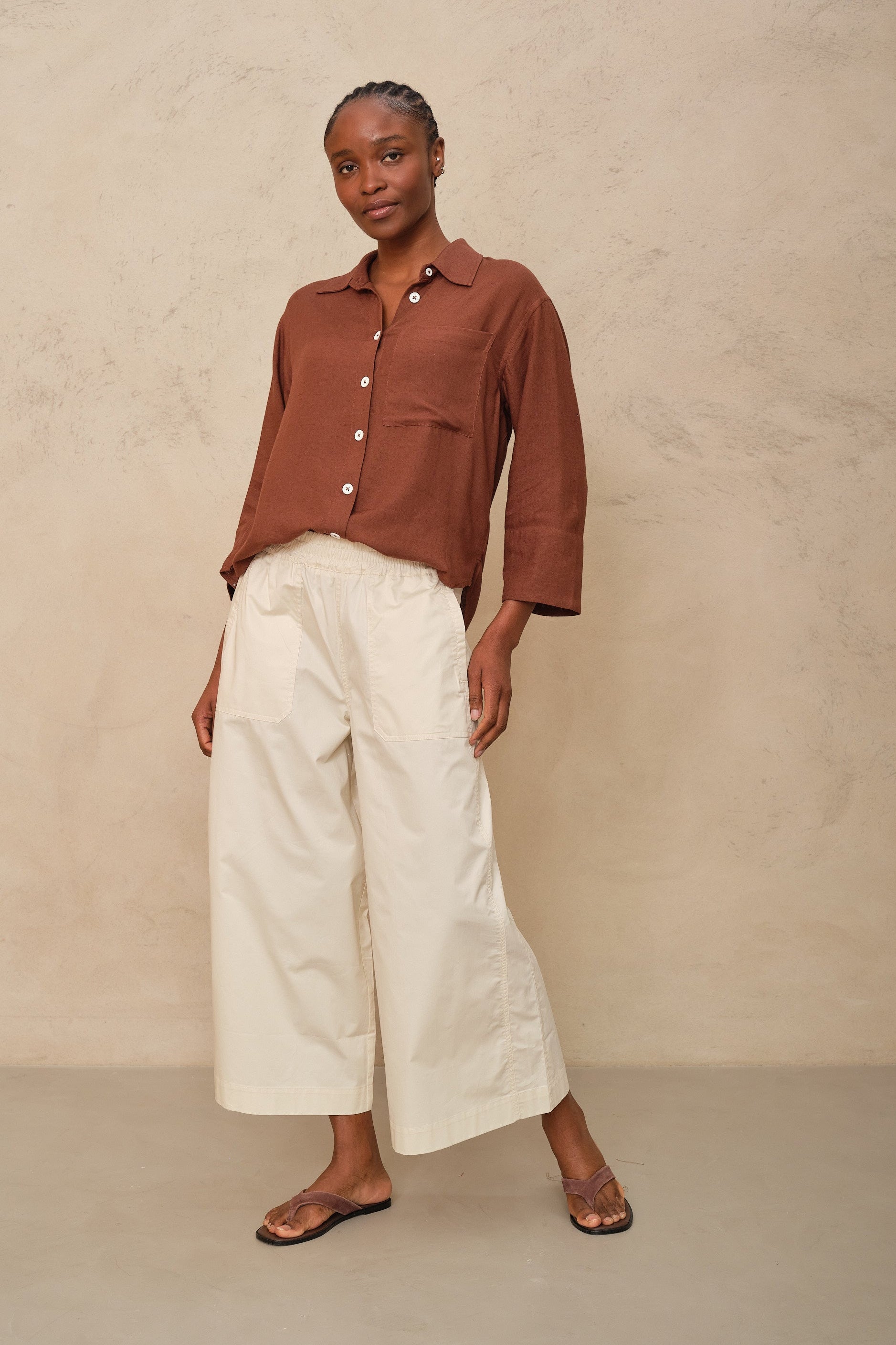 Woman wearing a brown blouse and white pants against a beige background