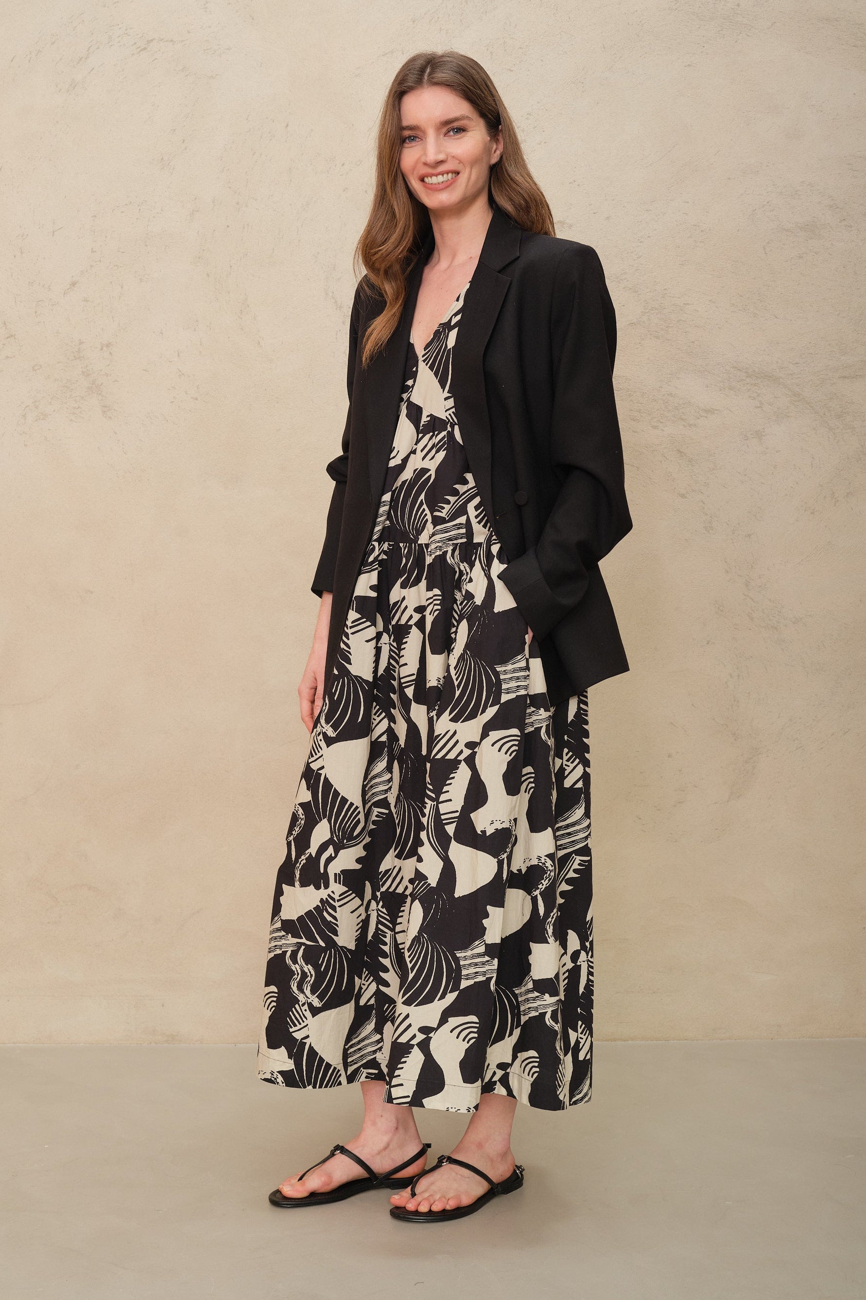 Woman wearing a black and white patterned dress with a black jacket against a beige background