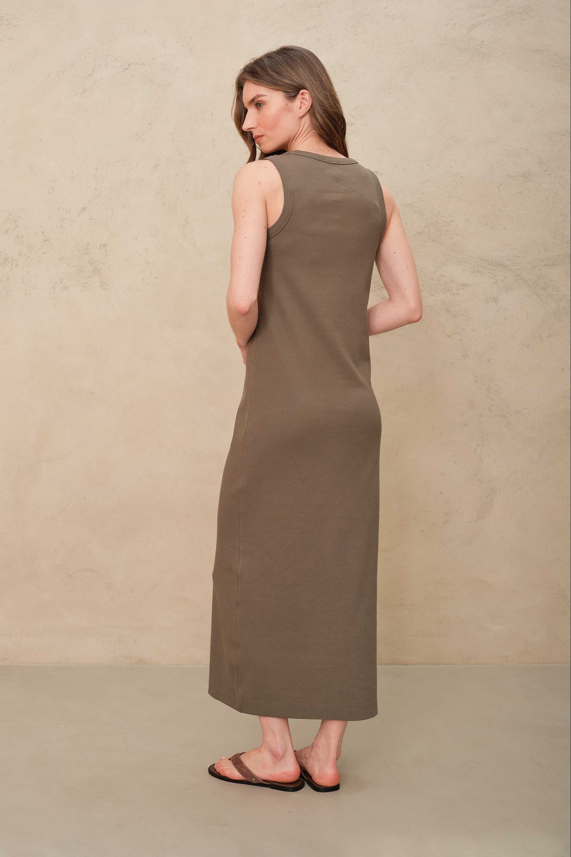 Woman wearing a long brown dress against a beige background