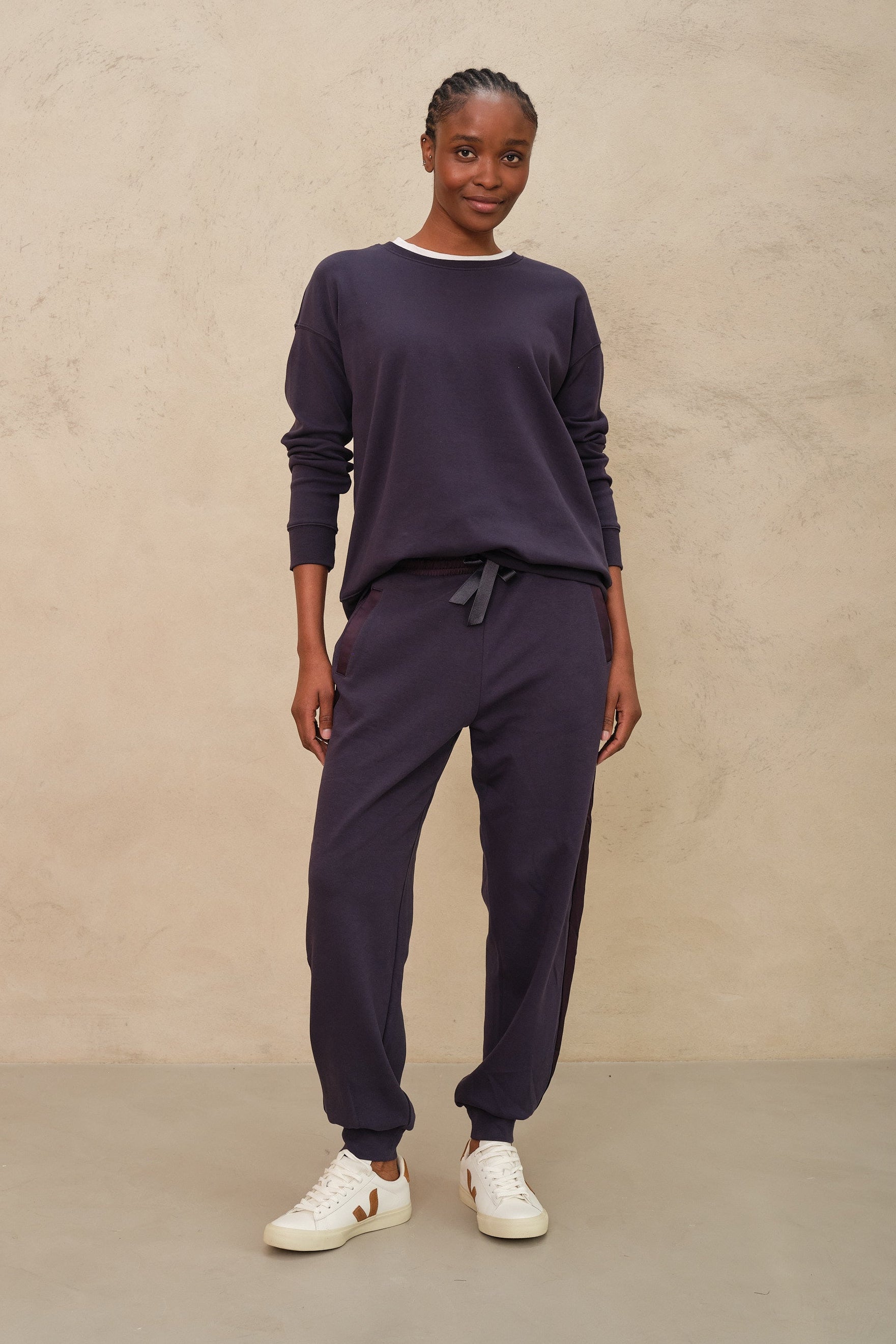 Person wearing a navy outfit with white sneakers against a beige background