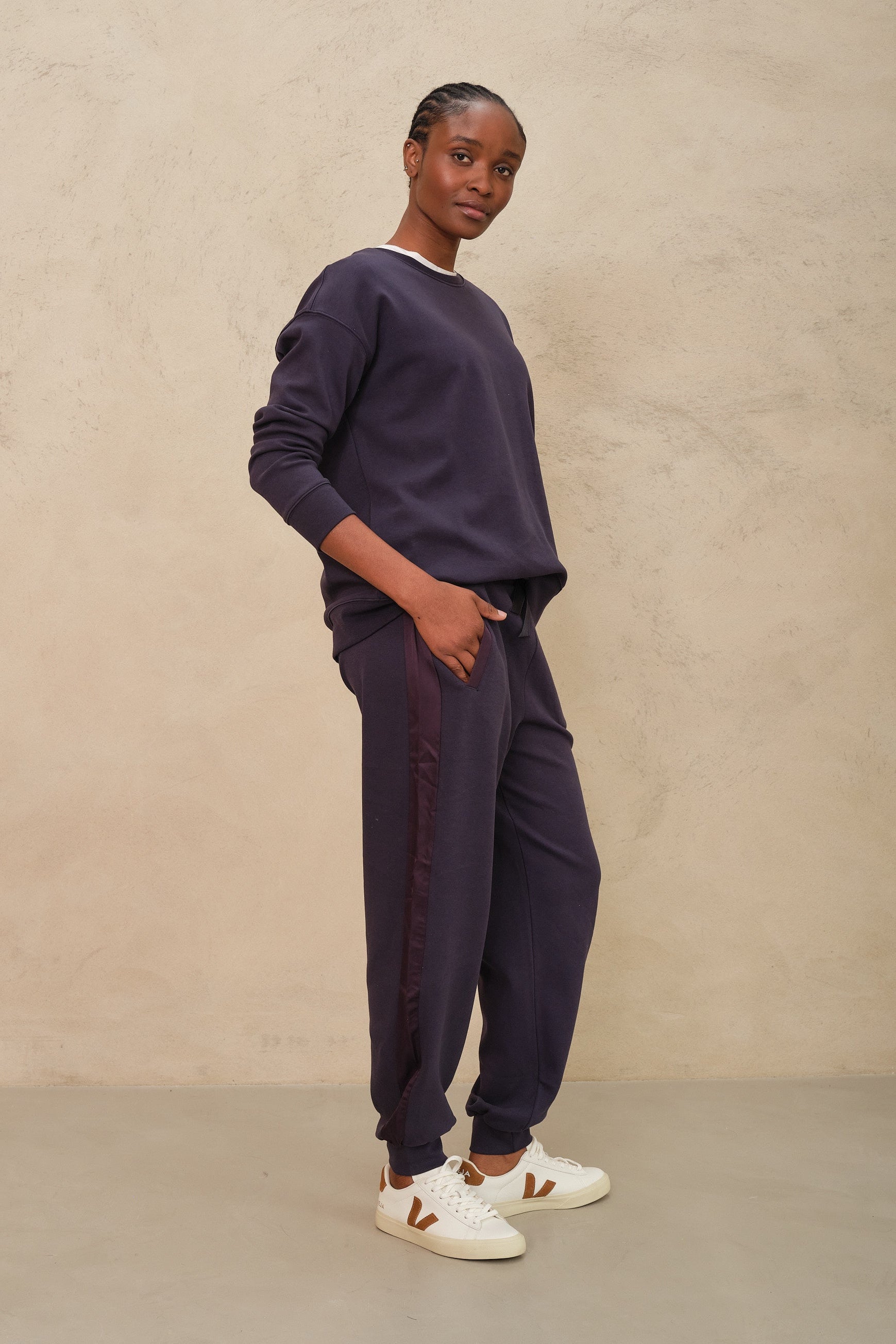 Person wearing a navy sweatshirt and pants with white shoes against a beige background