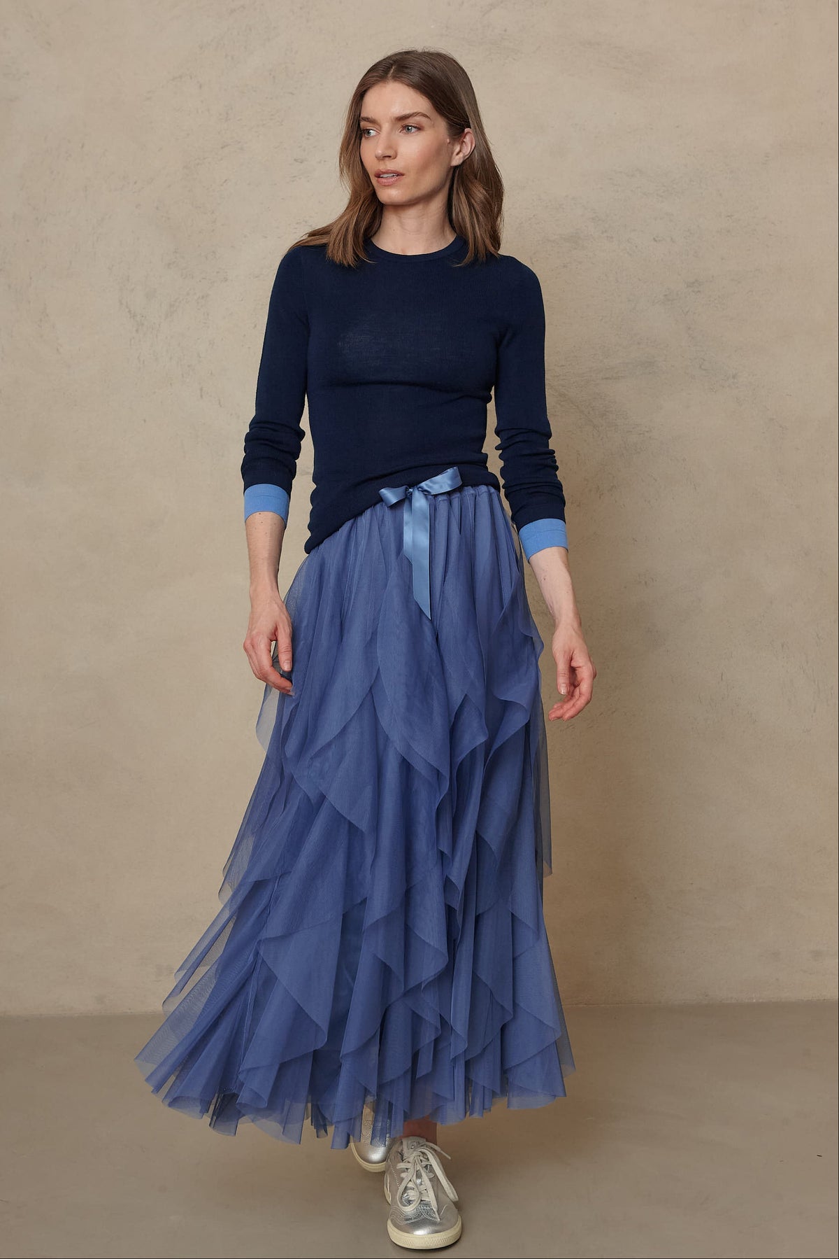 Model in the Iris tulle maxi skirt in lapis blue with a navy knit and silver trainers