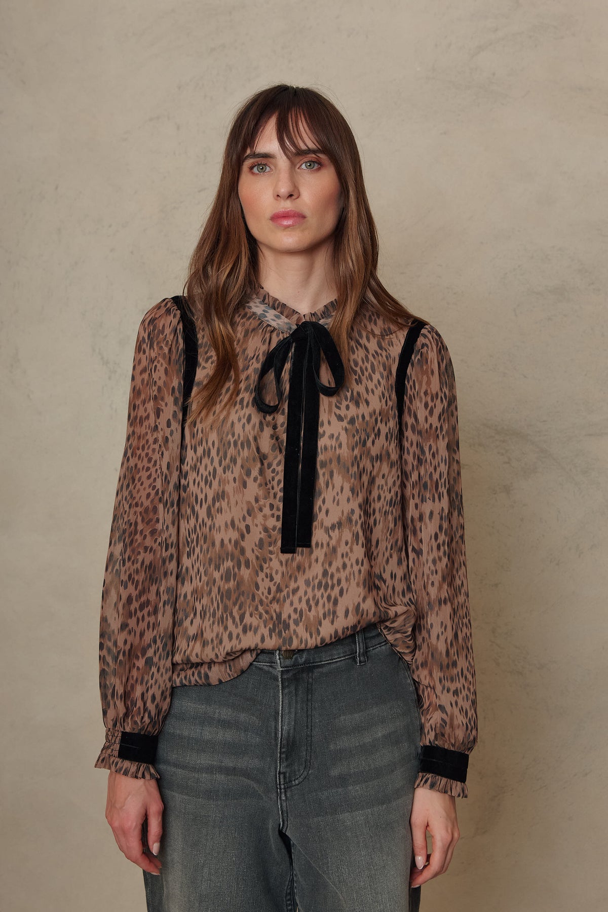 Jules animal print blouse with a black velvet tie neck and velvet trim, tucked into grey denim jeans, front view