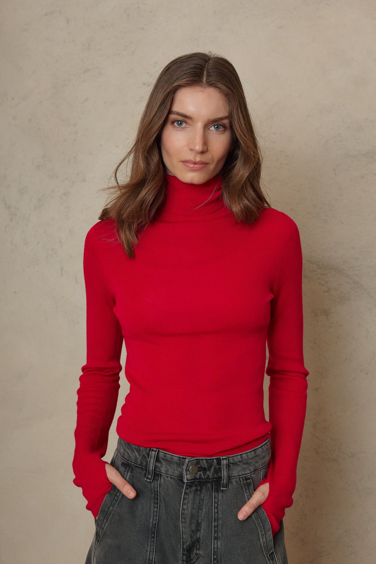 Close up of the Gwyneth fine merino roll neck in red tucked into grey jeans