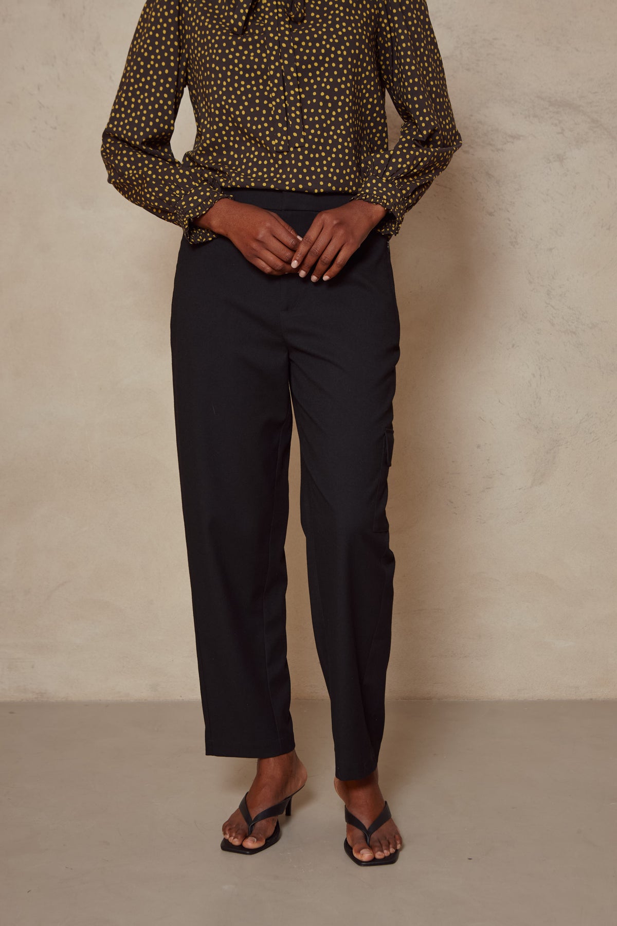 Front view of the Tess clean cargo trousers in black from the waist down, worn with sandals