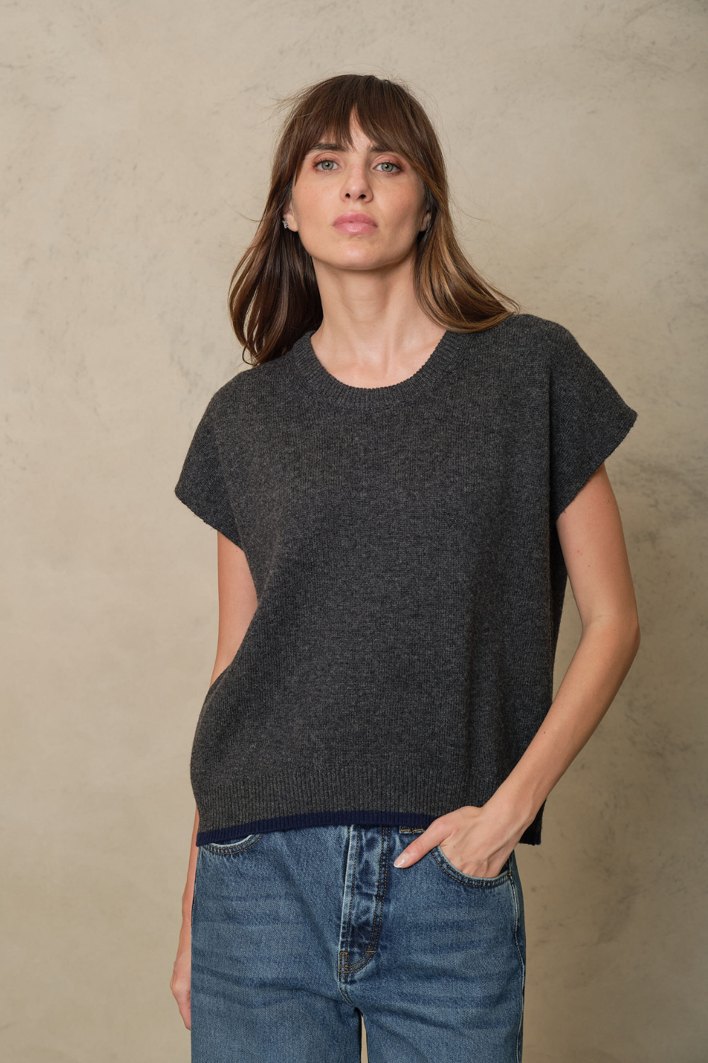 Ora charcoal knitted vest with a navy contrast hem, worn with blue jeans, front view