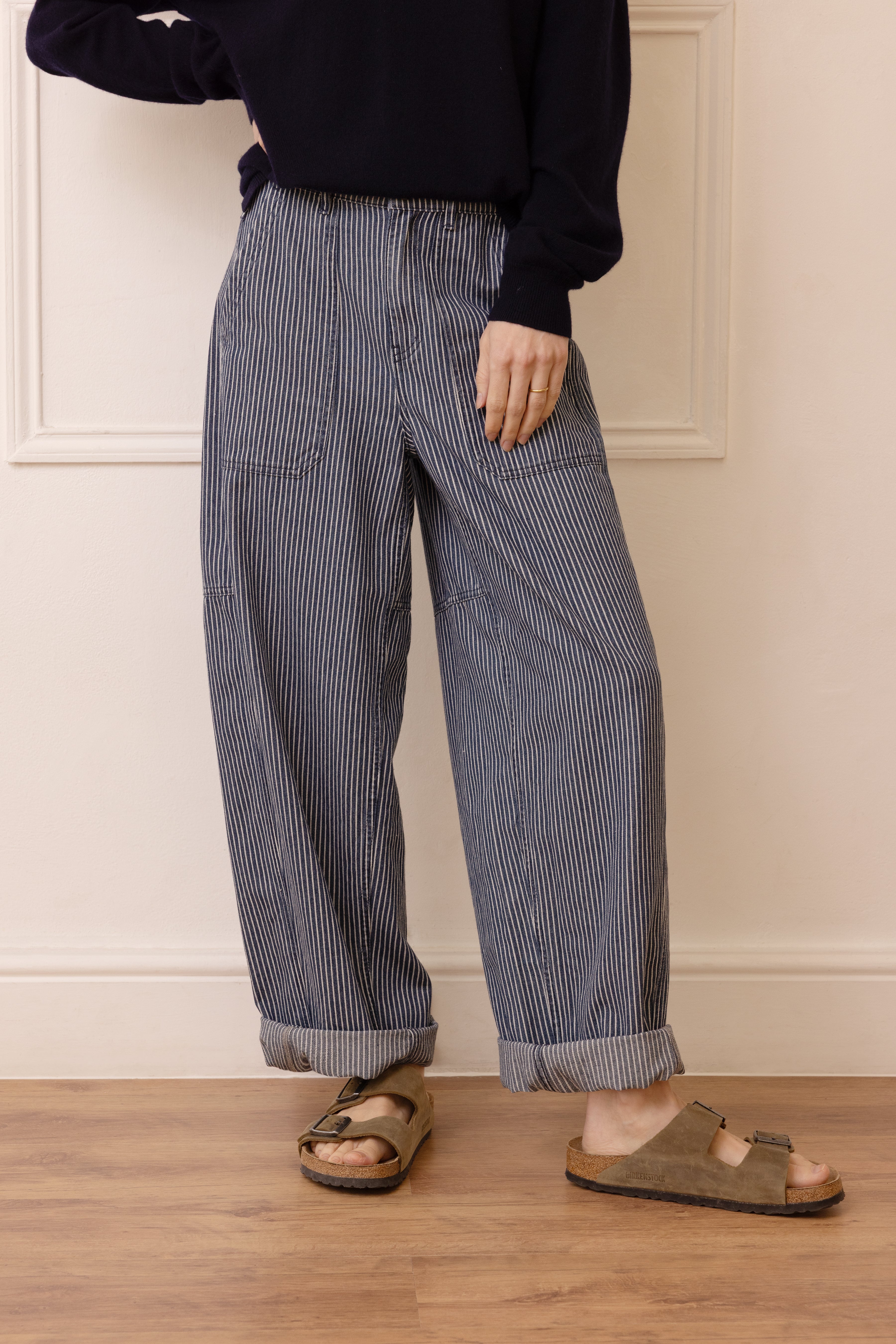 Person wearing blue striped pants and sandals standing on a wooden floor.