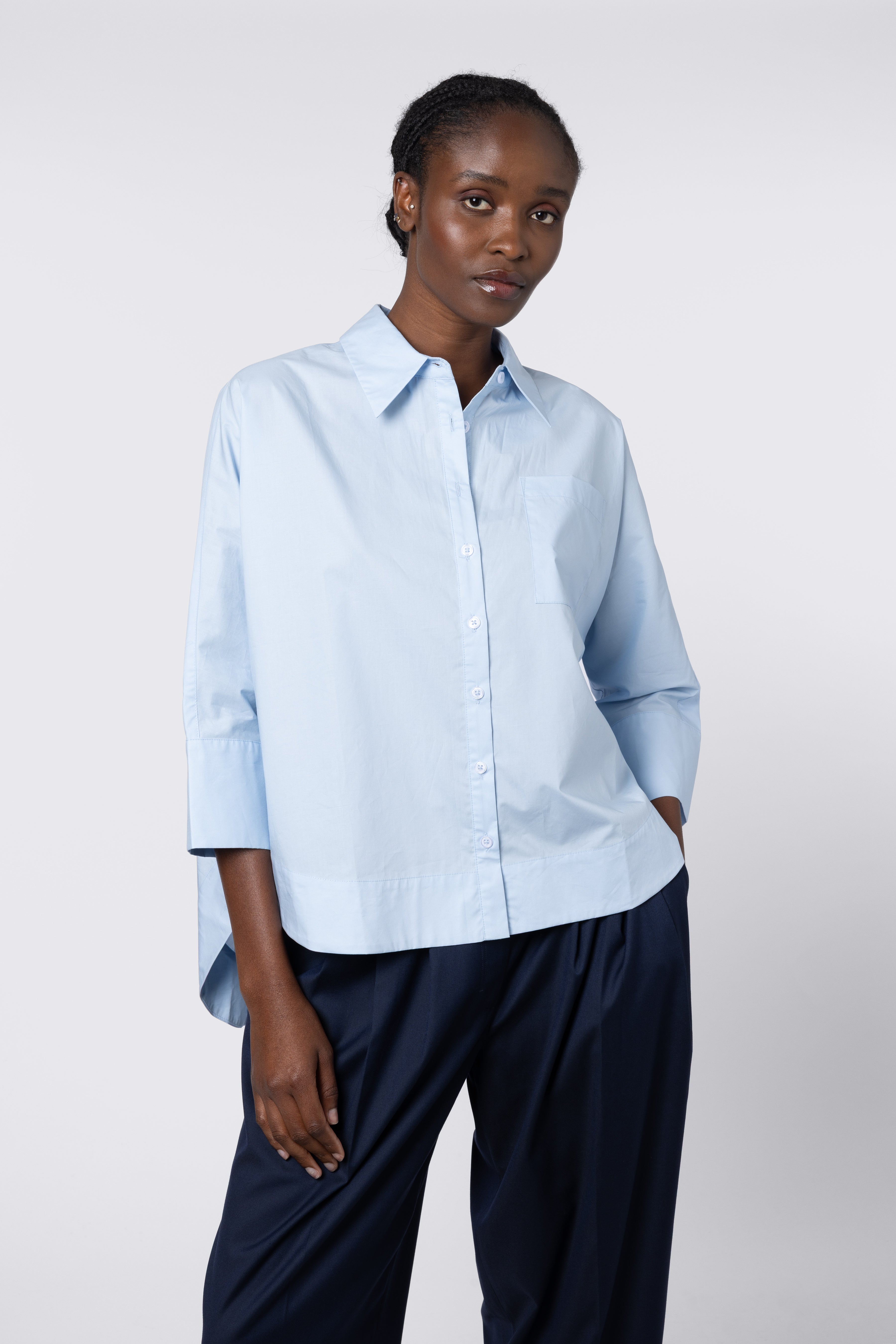 Woman wearing a light blue shirt and dark pants against a white background