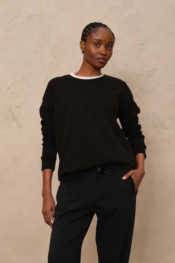 Person wearing a black outfit with white sandals against a beige background