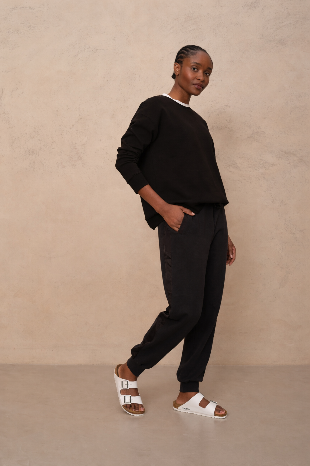 Person wearing a black outfit with white sandals against a beige background