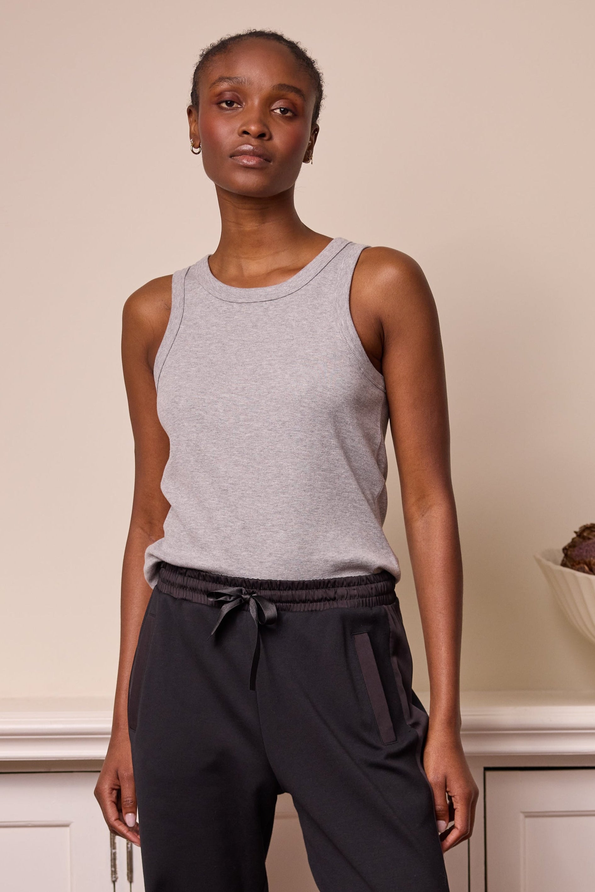 A model wearing a sleeveless grey ribbed vest and black joggers with a drawstring waist.
