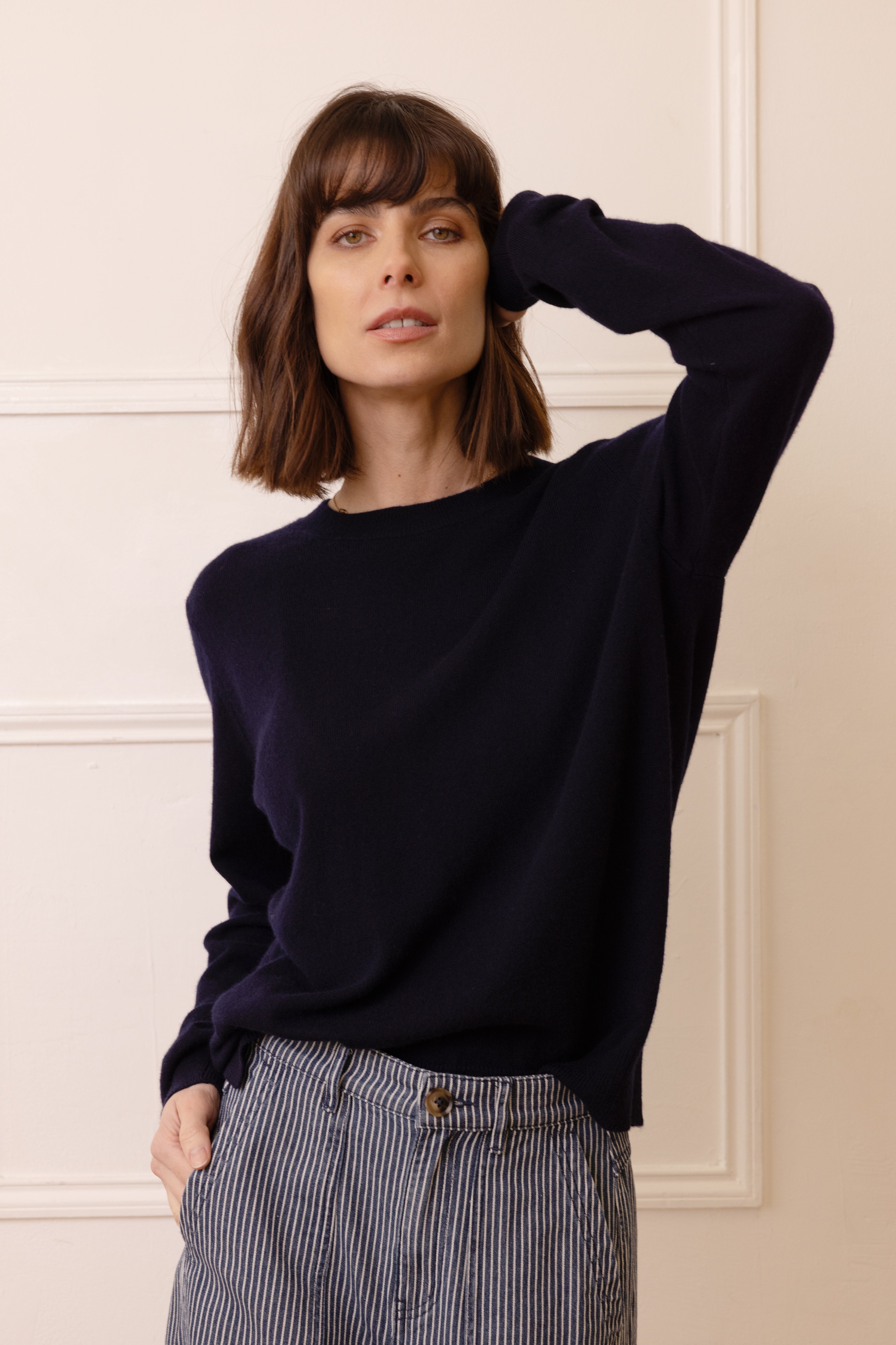 Woman wearing a black sweater and striped pants against a beige wall.