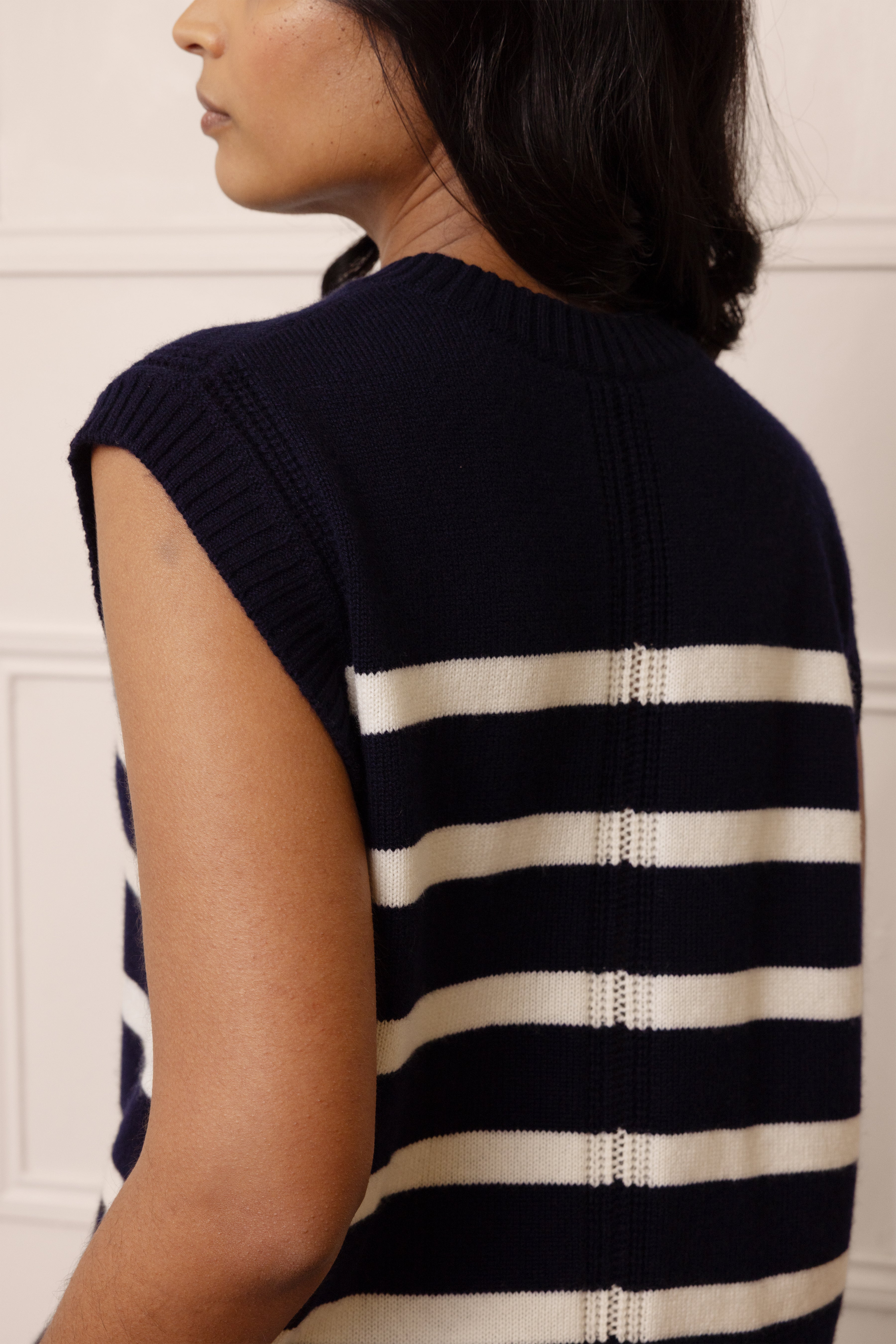 Navy and white striped sleeveless sweater worn by a person against a white wall.