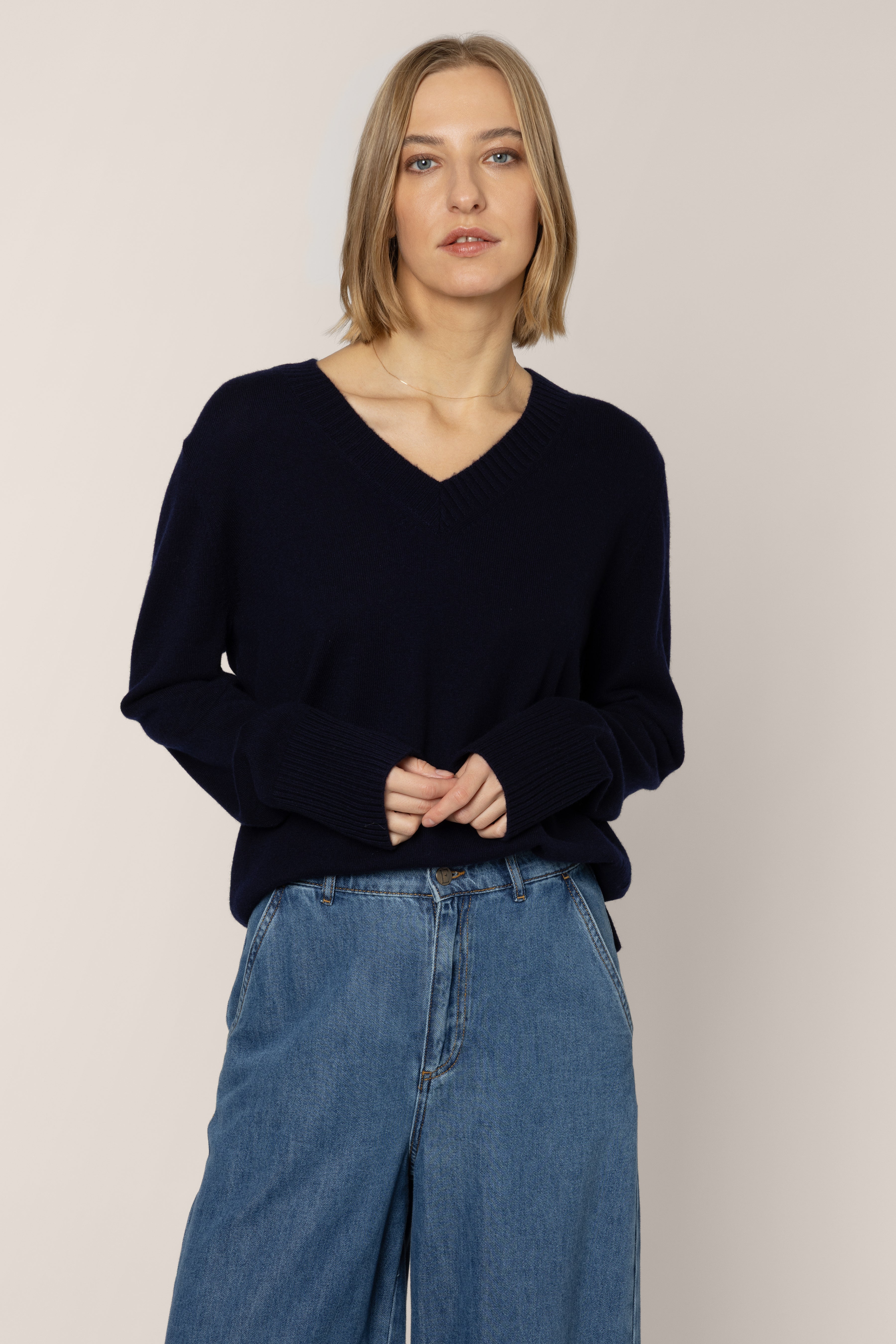 Woman wearing a black sweater and blue jeans against a plain background