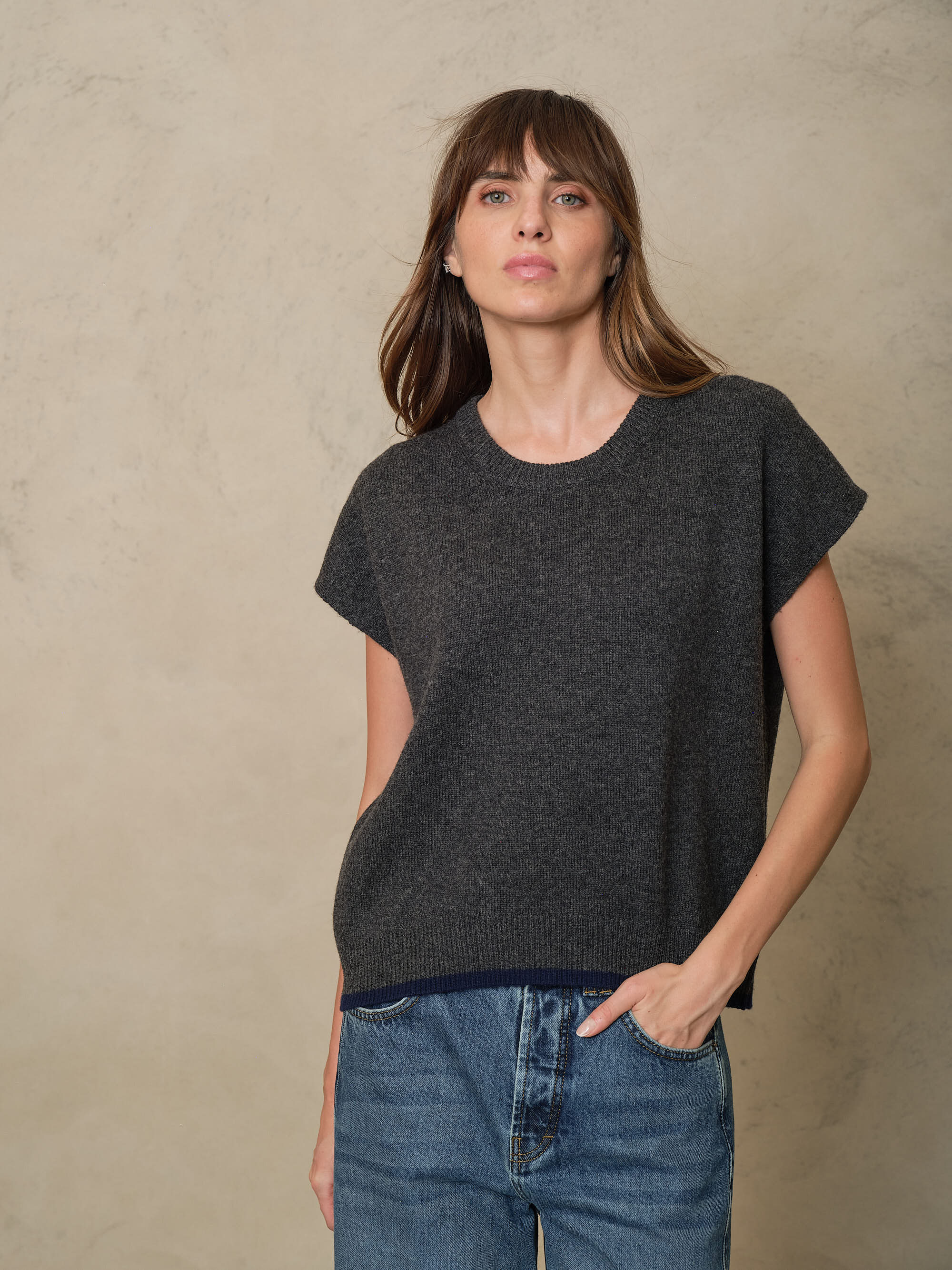 Model wearing the Ora knitted vest in charcoal with blue jeans, front view with hands in pockets