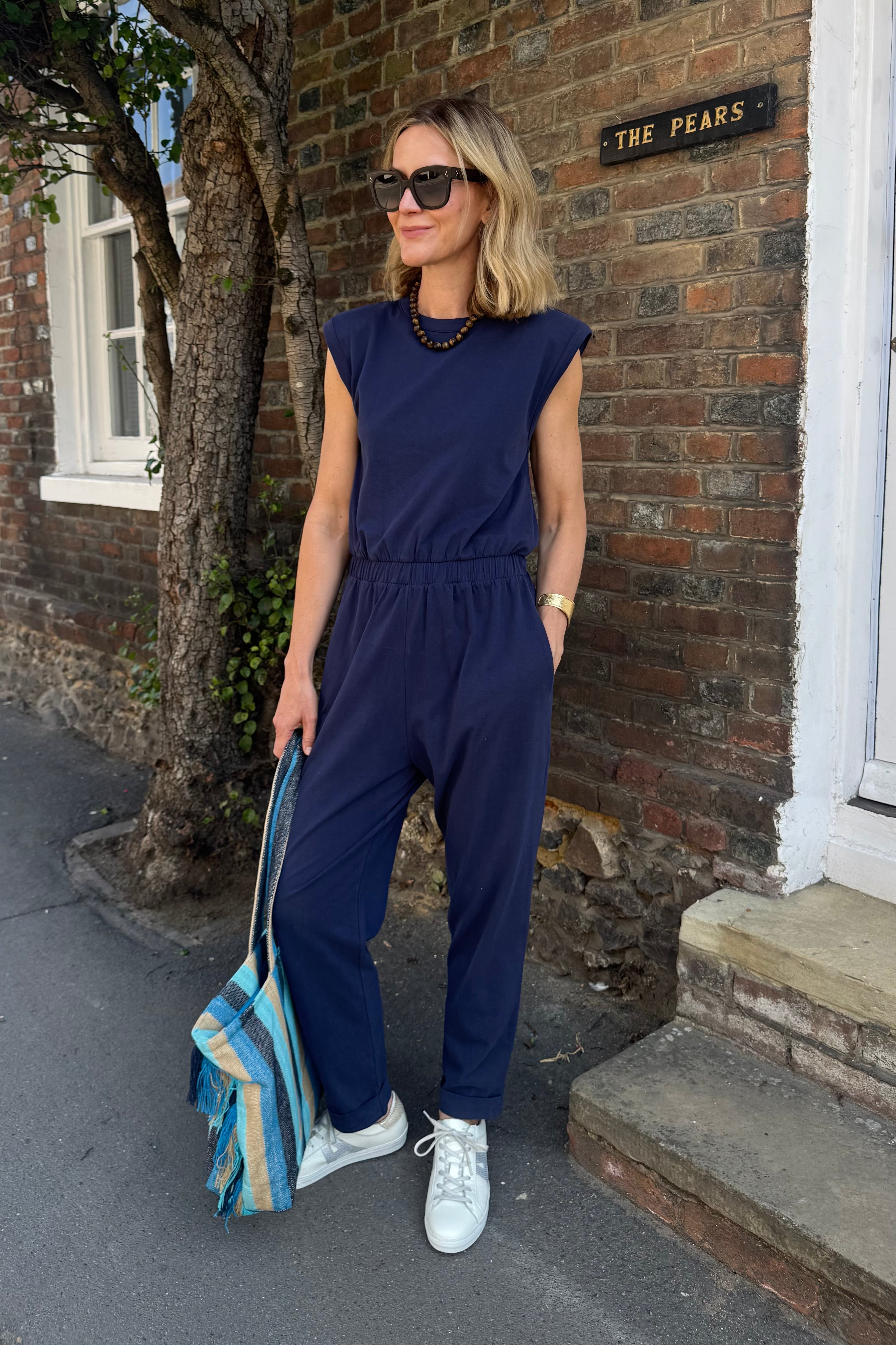 Woman in a navy jumpsuit standing outside a brick building