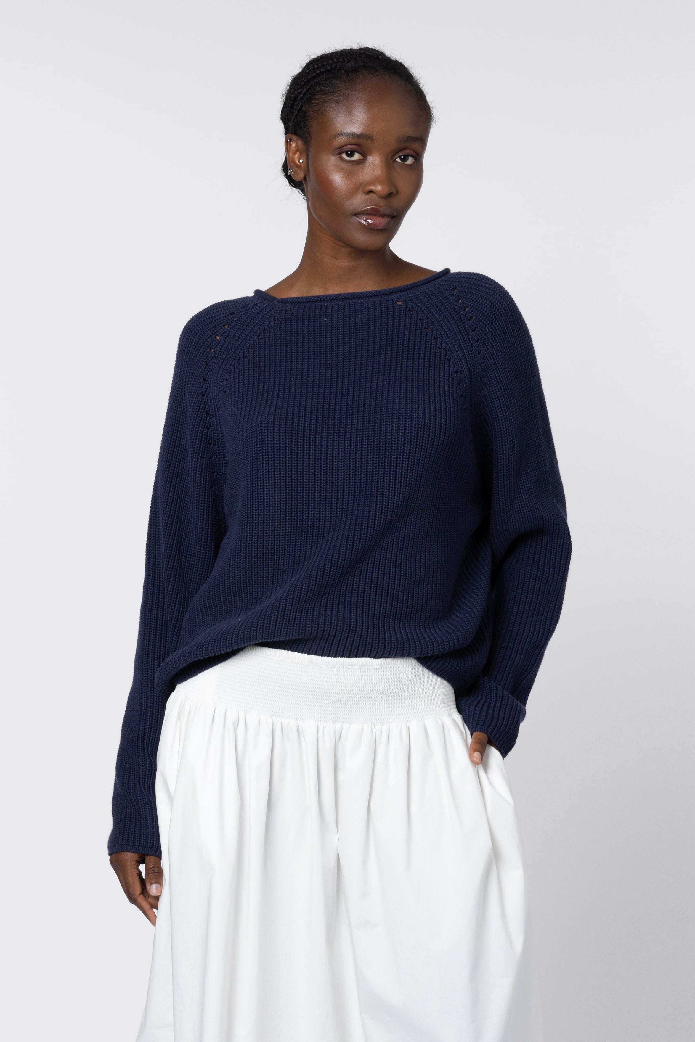 Woman wearing a navy sweater and white skirt on a white background