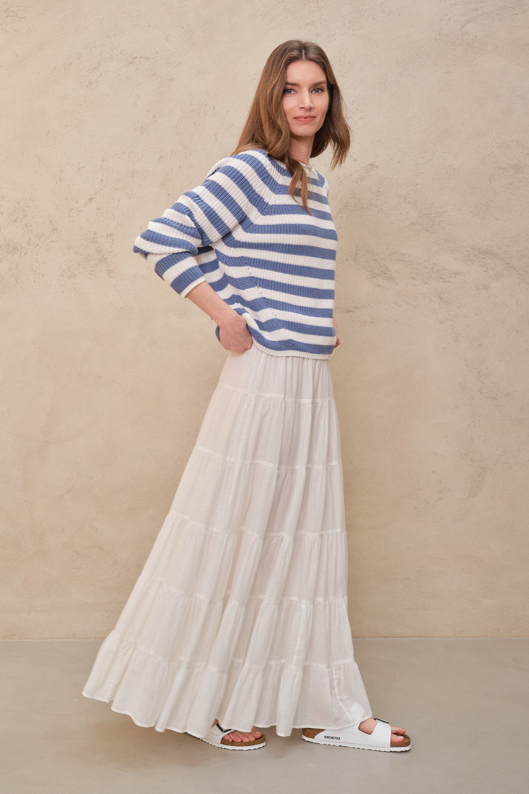 Woman wearing a blue and white striped sweater and white skirt against a beige background