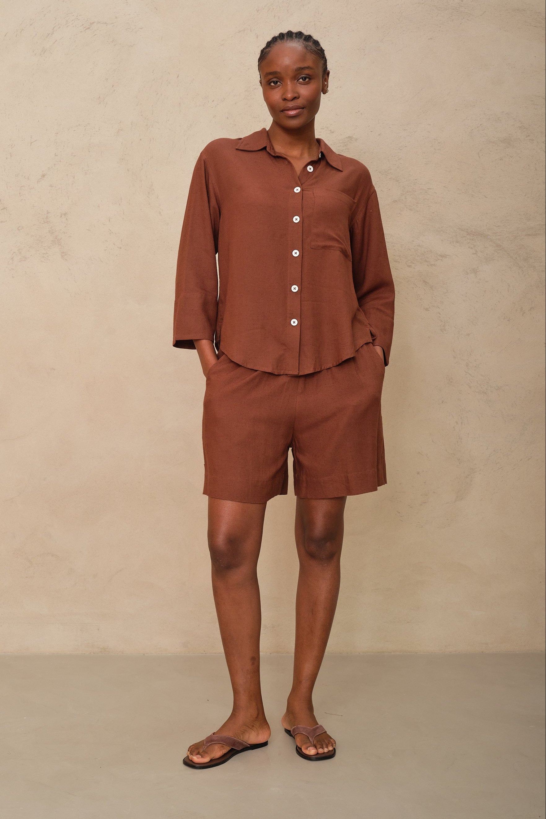Person wearing a brown button-up shirt and shorts set against a beige background