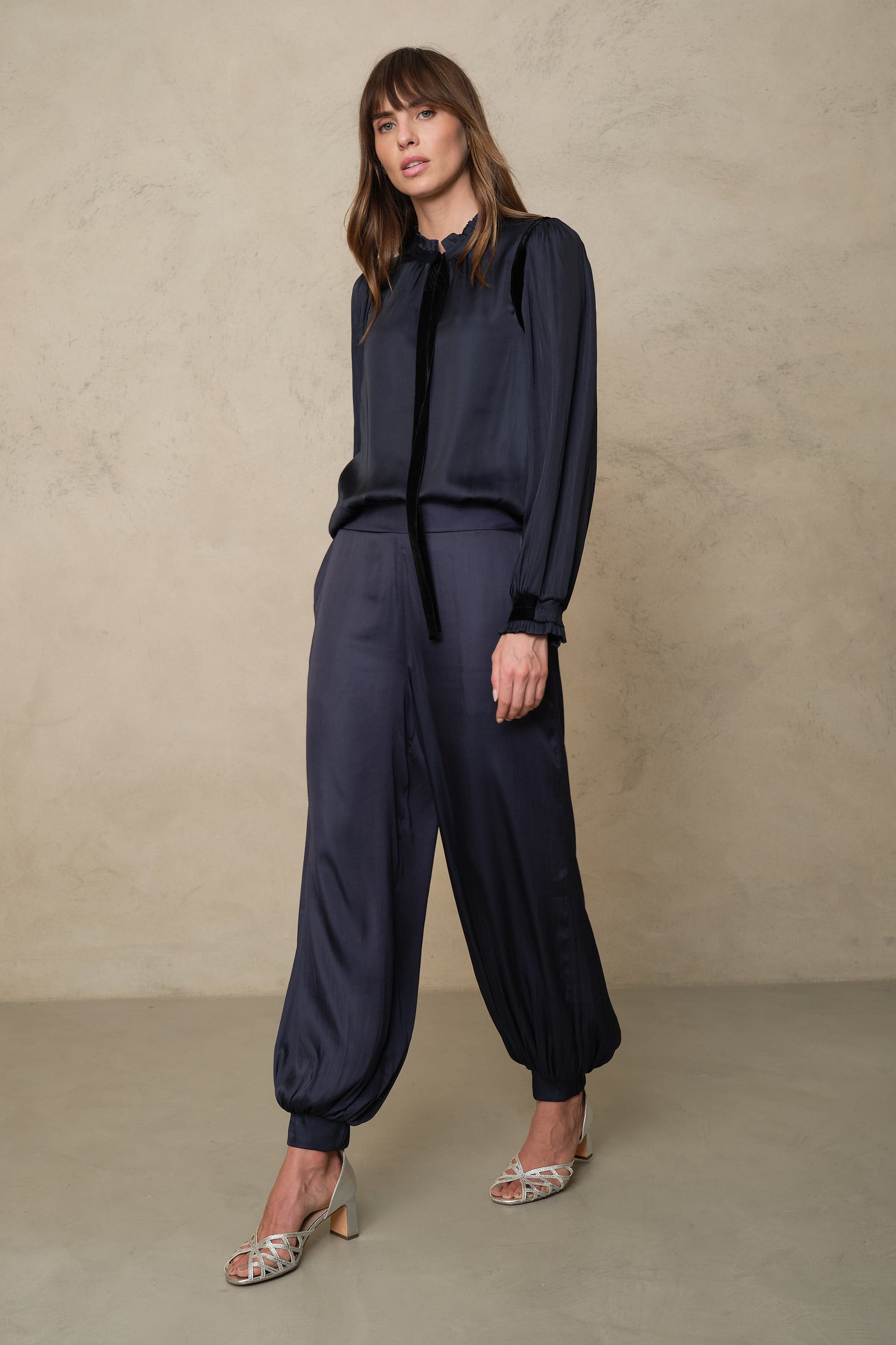 Maeve navy balloon trousers worn with a navy tie neck blouse and silver heeled sandals