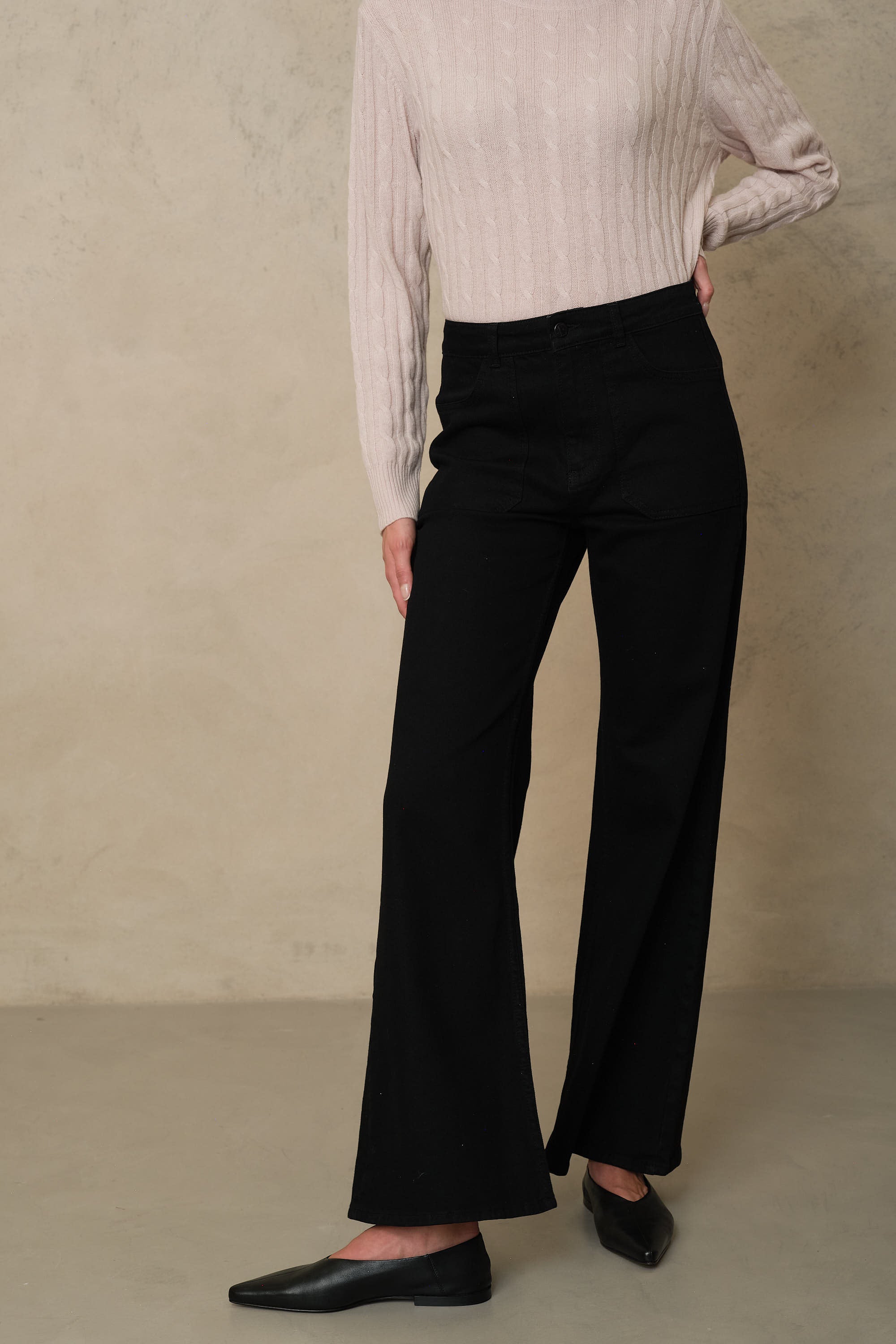 Black wide leg jeans with a high waist, worn with a pale pink cable knit and black flats