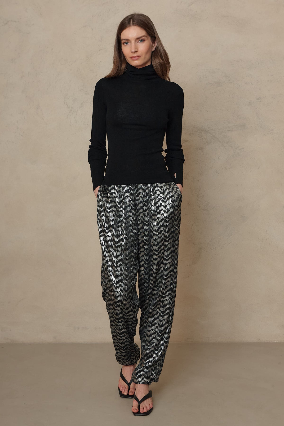 Silver metallic trousers worn with a black roll neck and heeled sandals