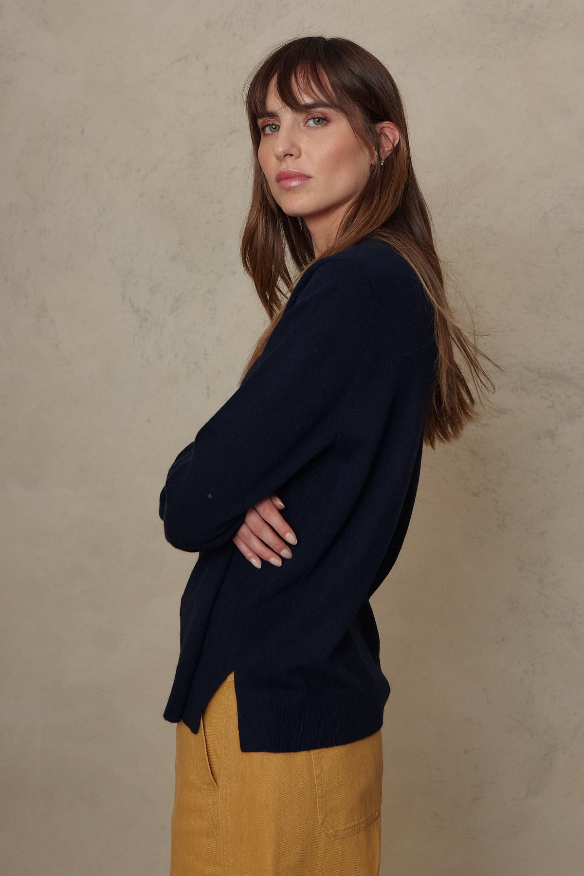 Side view of the Alex navy jumper showing the split hem, worn with mustard trousers