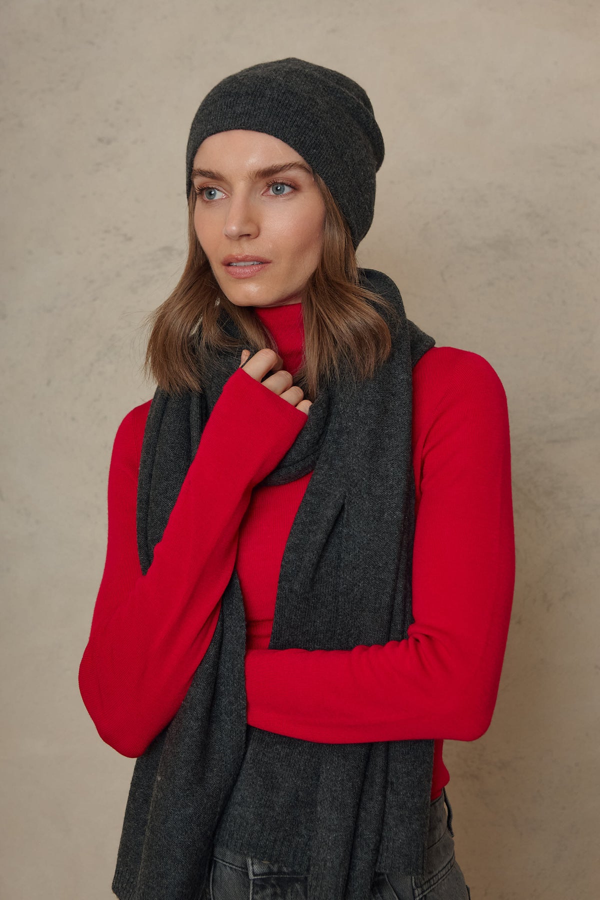 Model holding the Carmel cashmere blend scarf in charcoal up to her chin, worn with the Zinnie beanie in charcoal