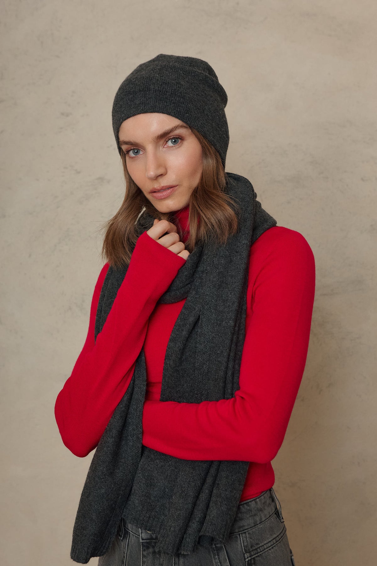 Carmel cashmere blend scarf in charcoal looped around the neck over a red knit, side view