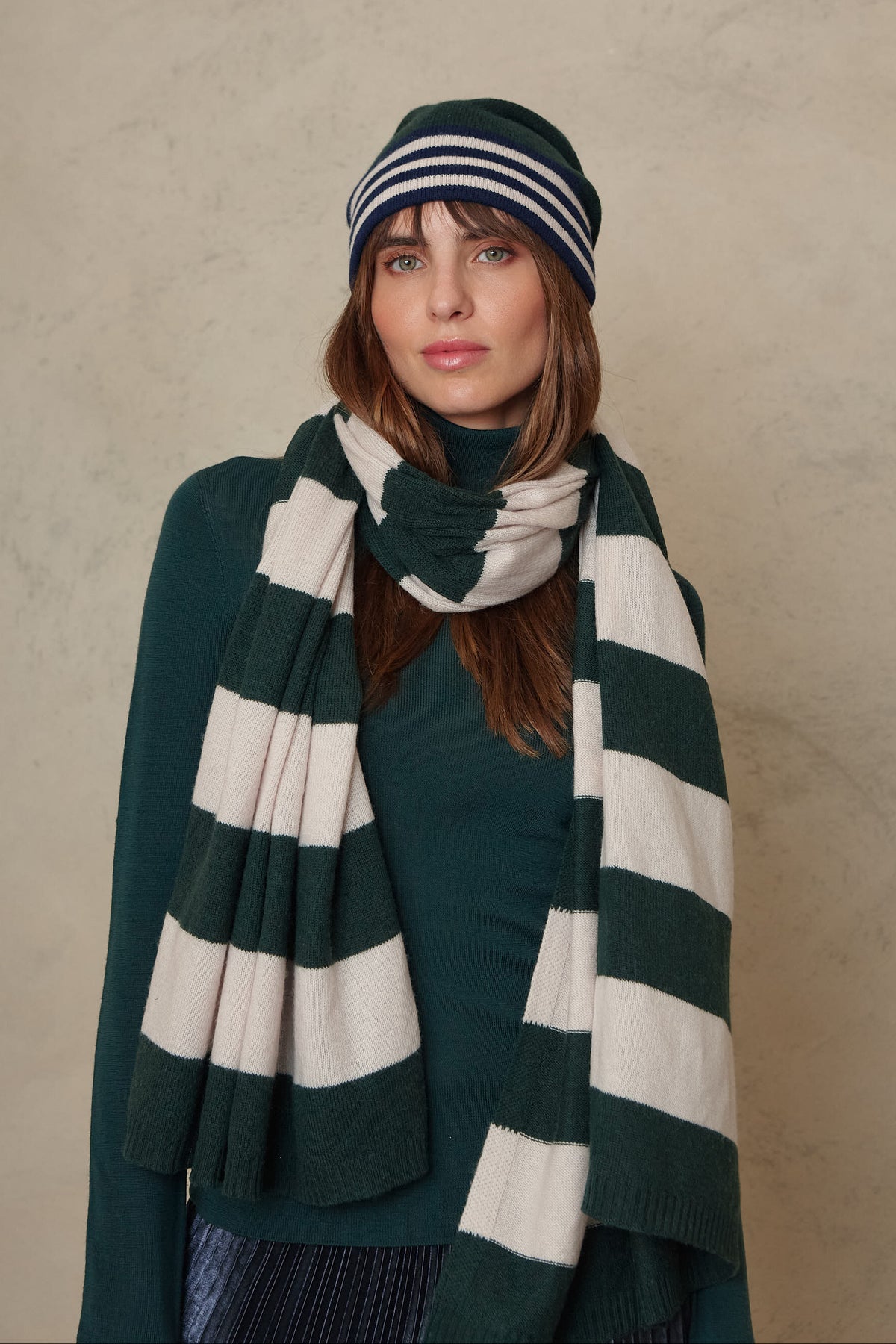 Model wearing the Carmel cashmere blend scarf in soft stone and bottle green stripes with the Zinnie beanie in bottle green, front view