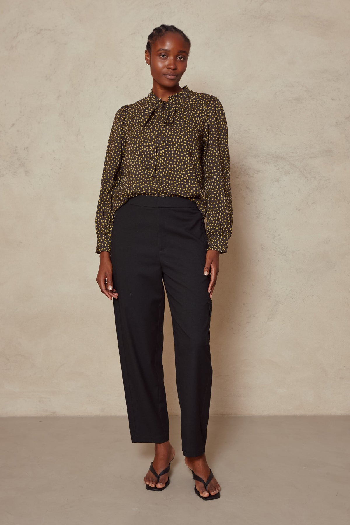 Model wearing the Tess clean cargo trousers in black with a spot print blouse tucked in, front view