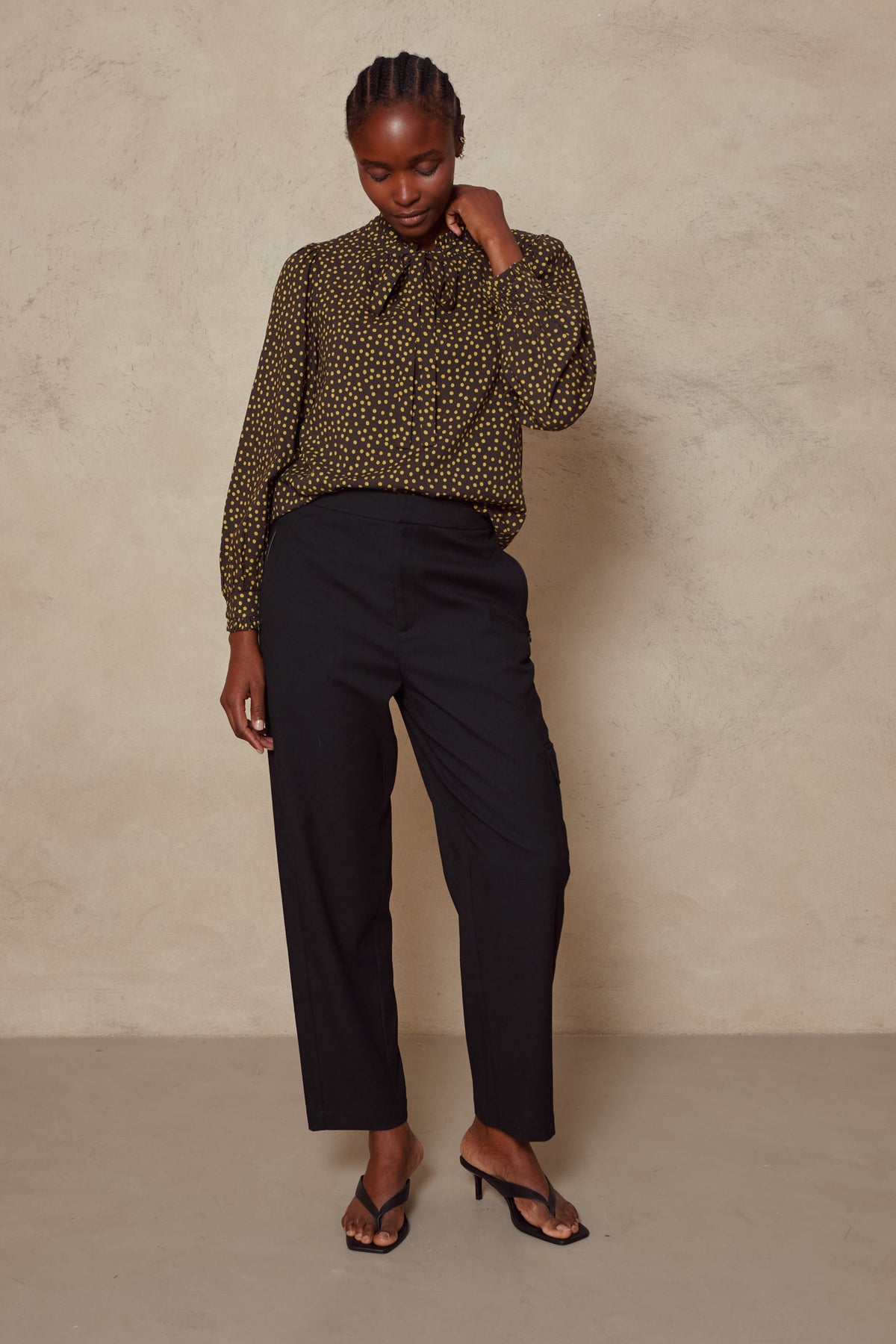Model wearing the Tess clean cargo trousers in black with a spot print blouse, full length front view