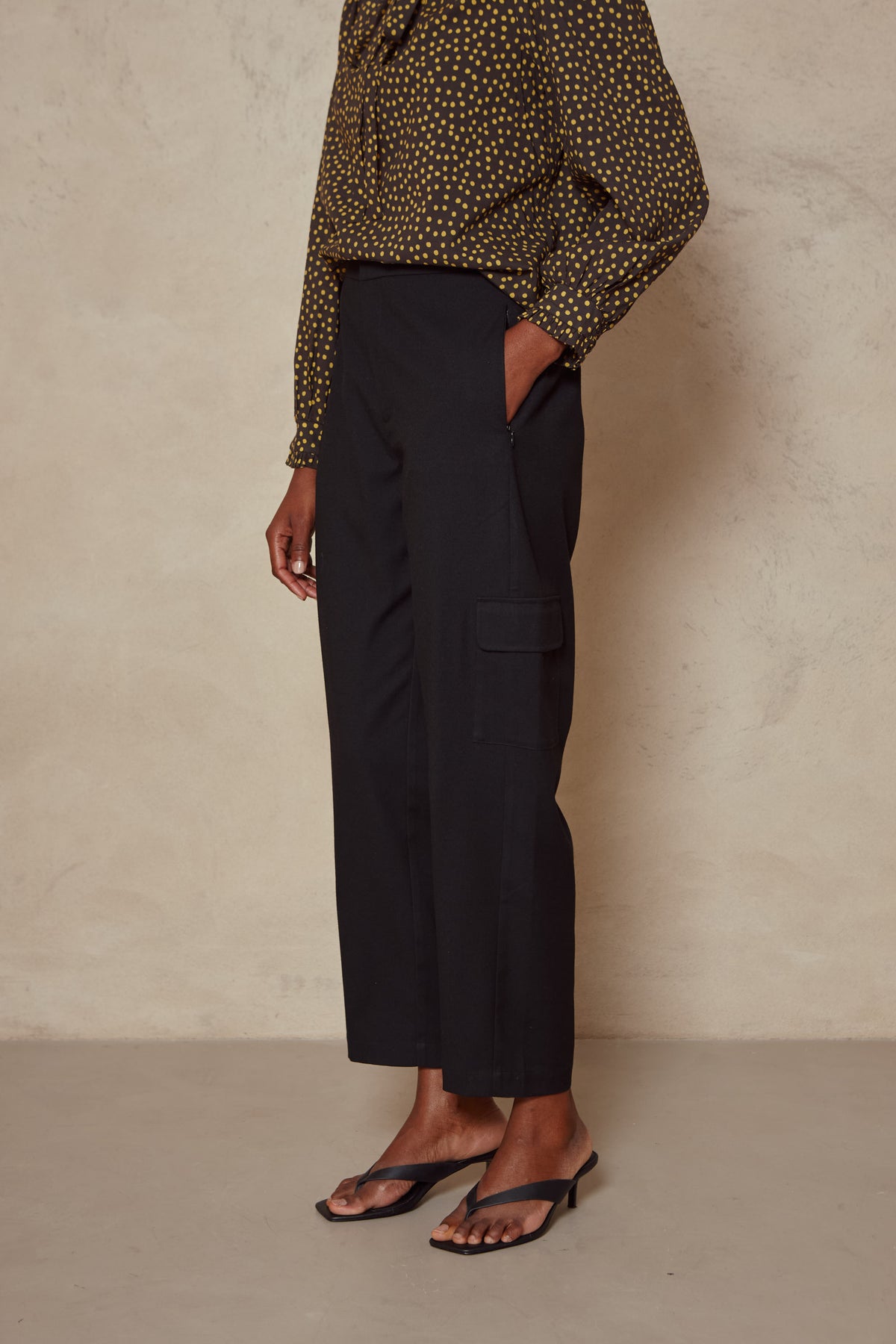 Side view of the Tess clean cargo trousers in black, worn with a spot print blouse and sandals