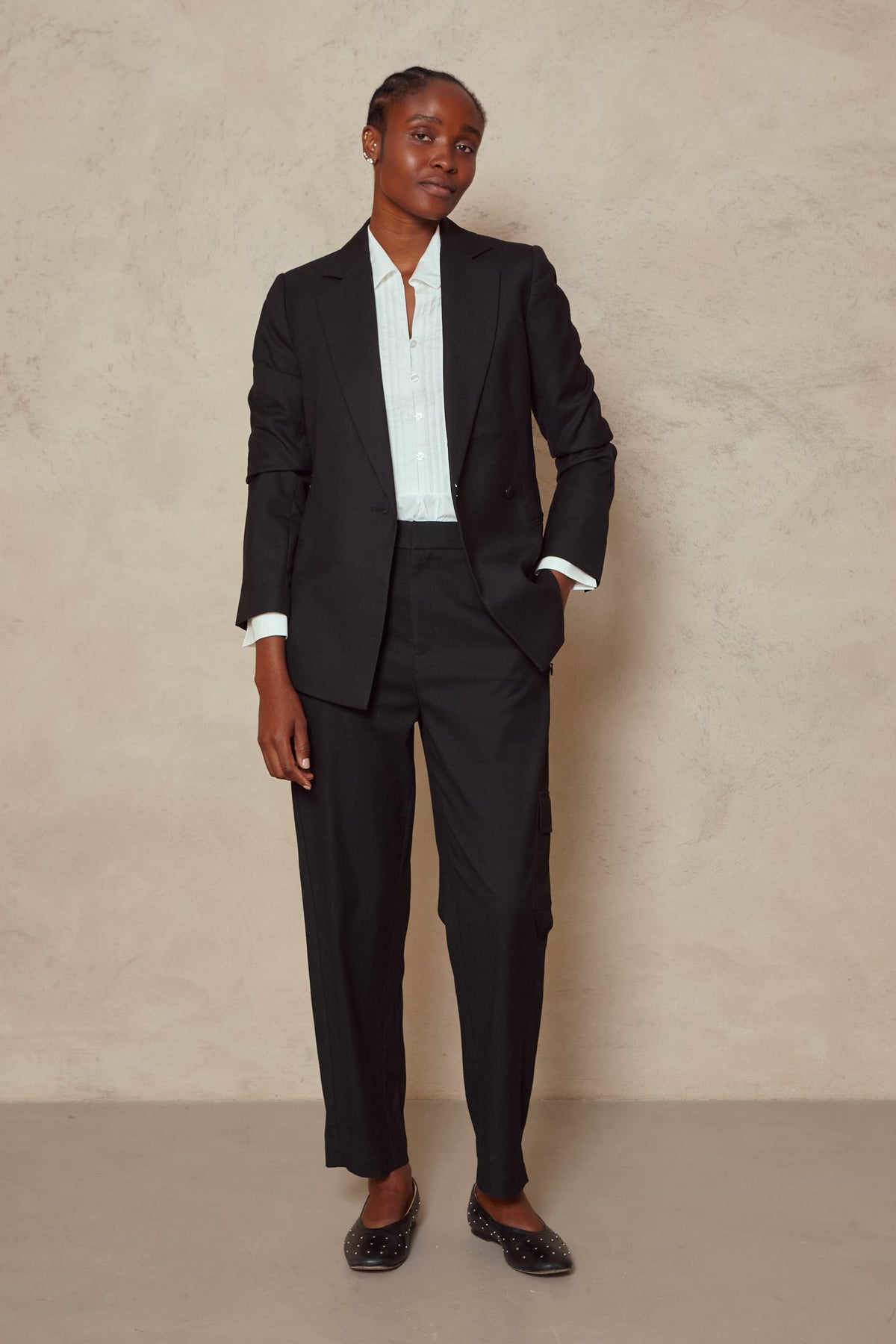 Model wearing the Tess clean cargo trousers in black with a black blazer and white shirt, front view