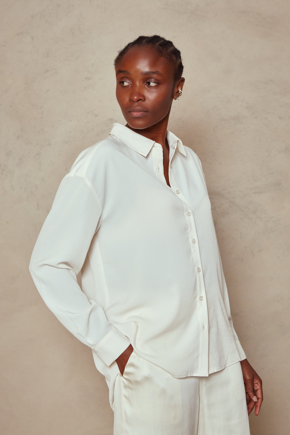 Model wearing the Margot shirt in ivory, three quarter view with one hand in her trouser pocket