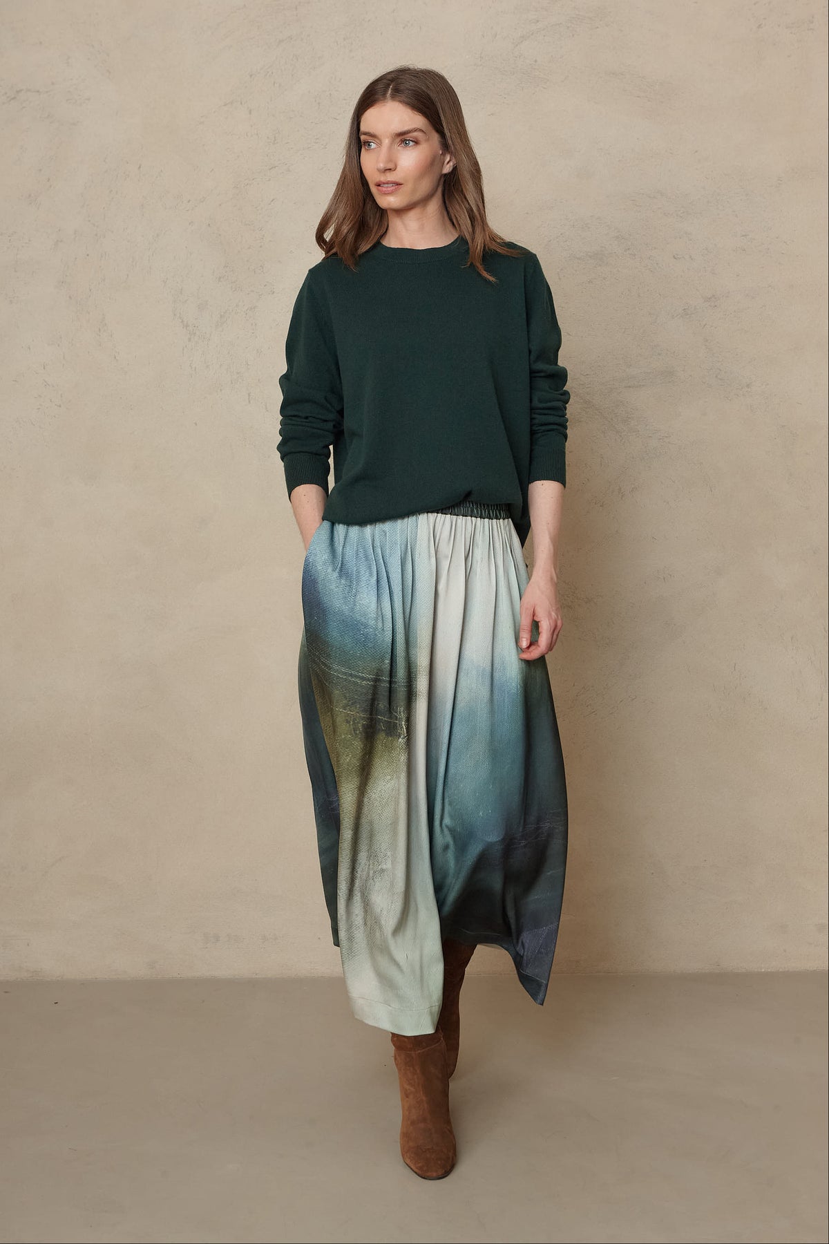 Full length view of the Alex jumper in bottle green with a printed midi skirt and brown boots