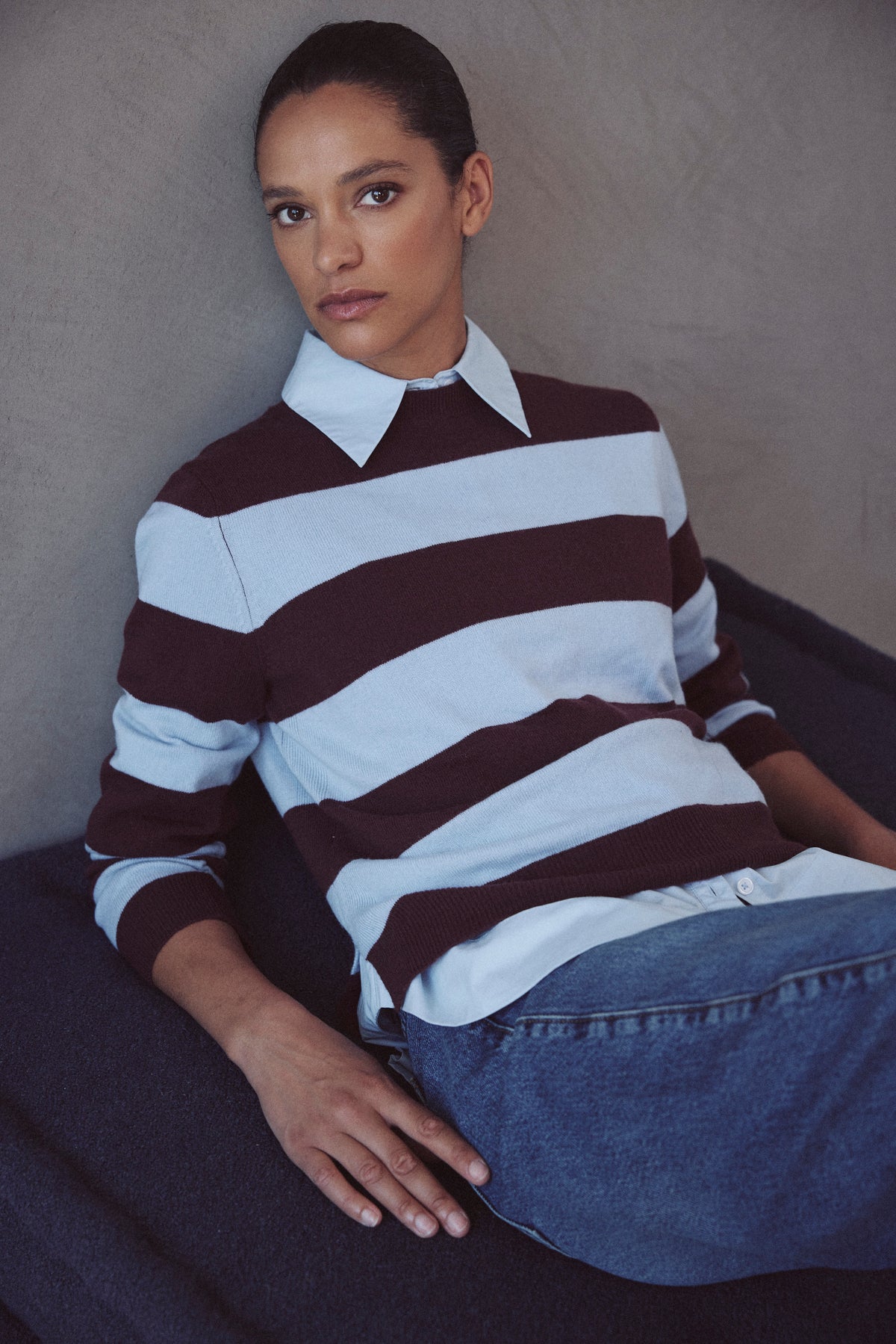 Sky blue and burgundy striped jumper worn over a collared shirt with denim