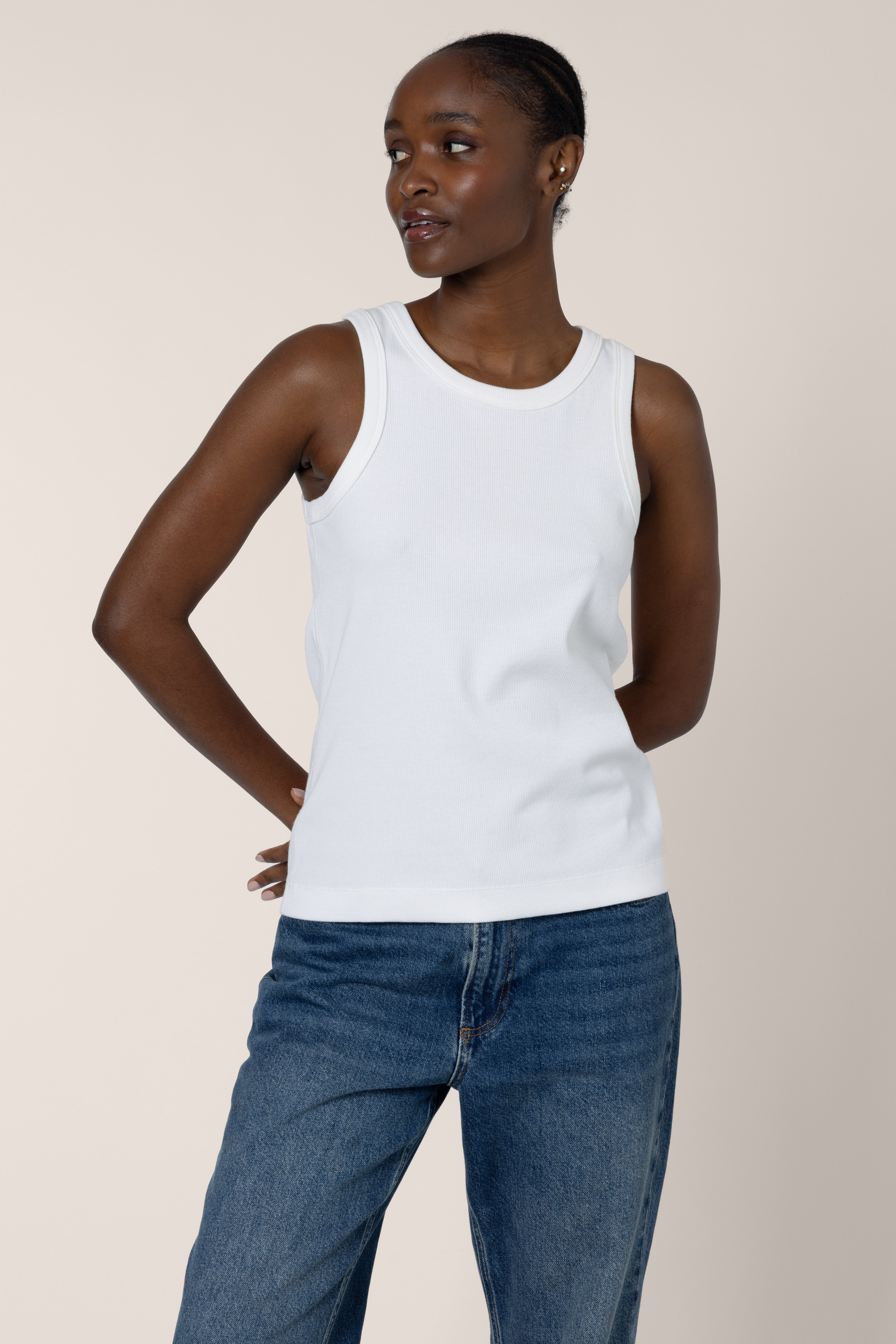 Woman wearing a white tank top and blue jeans against a plain background