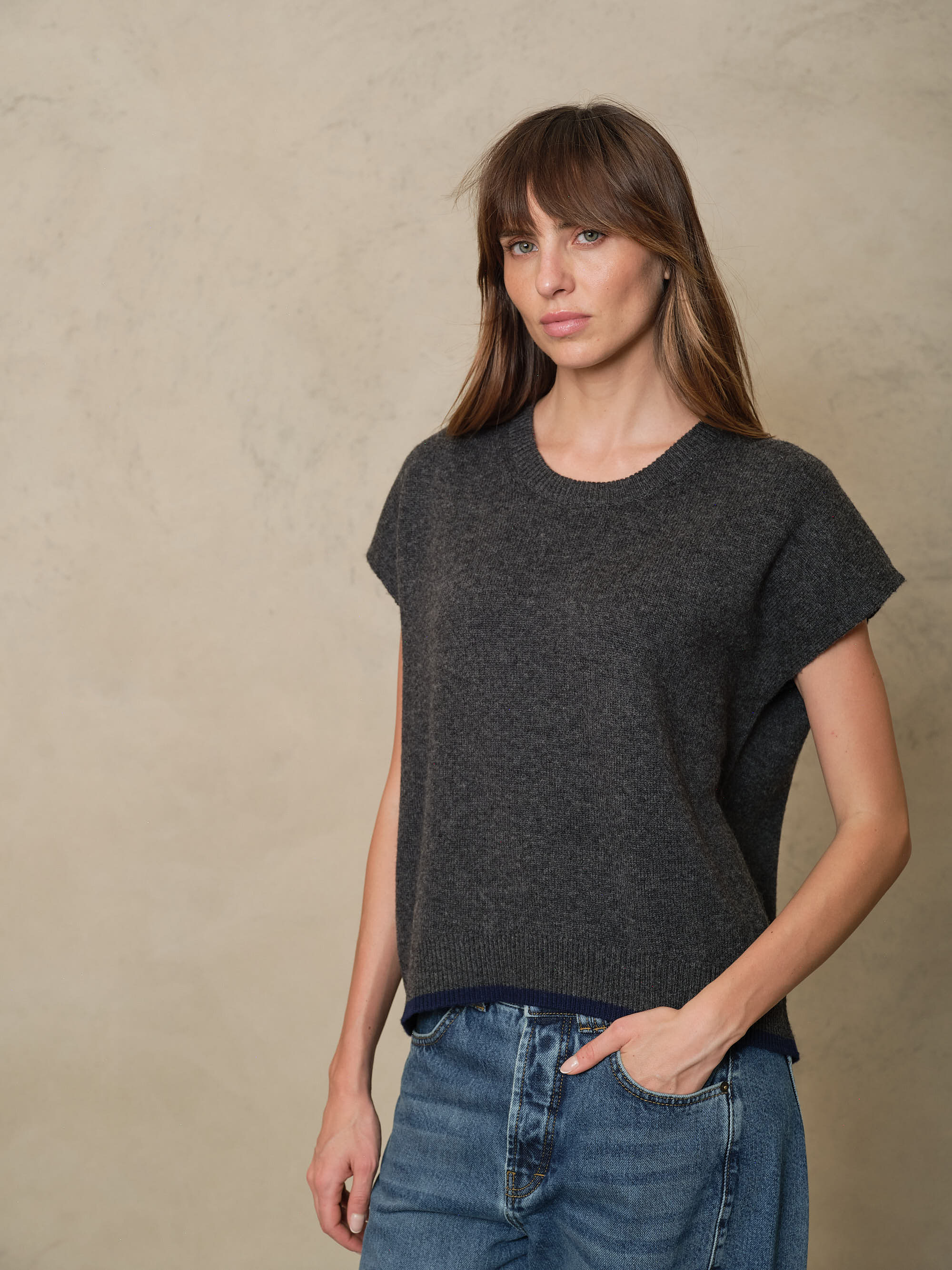 Ora charcoal knitted vest worn with blue jeans, front view showing the boxy body and cap sleeve