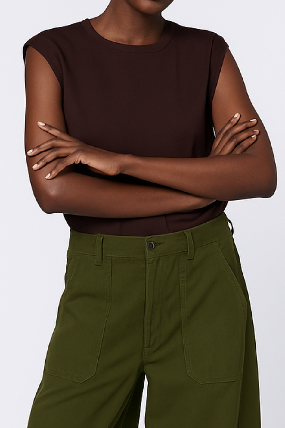 Person wearing a brown top and green pants with arms crossed on a white background