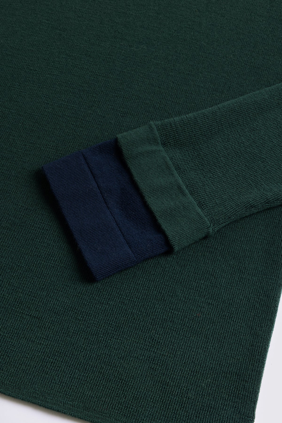 Bottle green merino crew neck jumper with a navy cuff, shown flat
