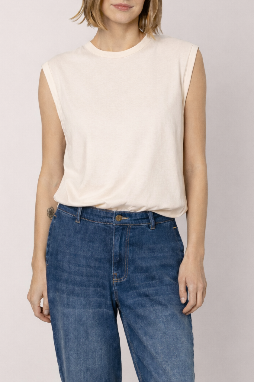 Person wearing a white sleeveless top and blue jeans on a plain background