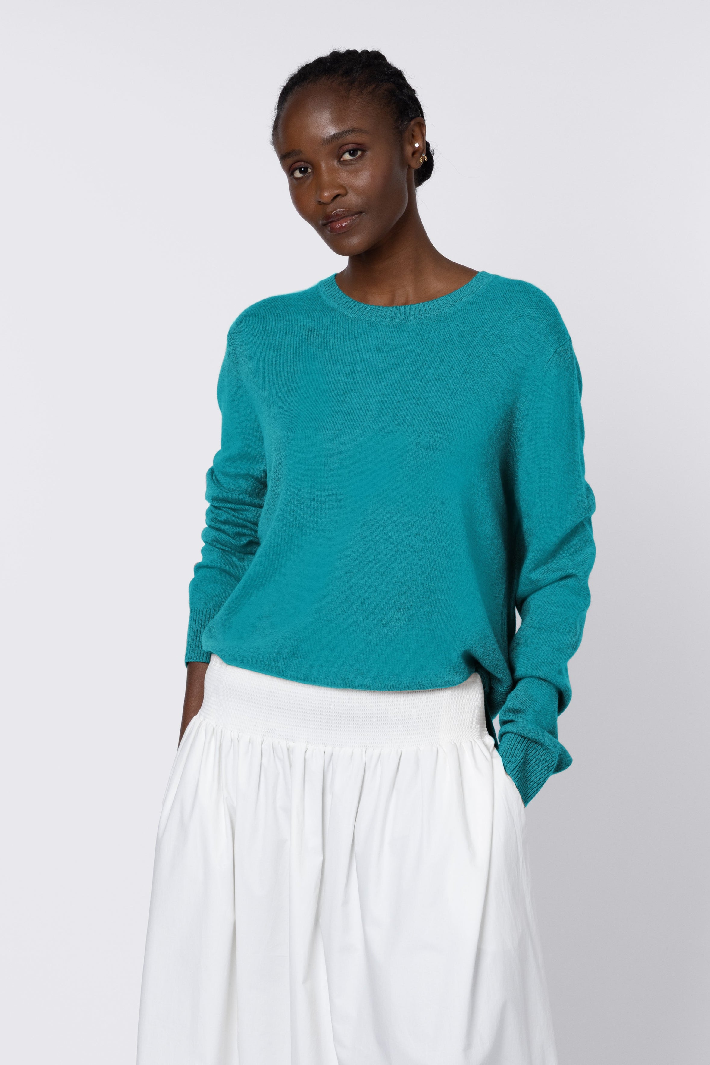 Woman wearing a teal sweater and white skirt on a white background
